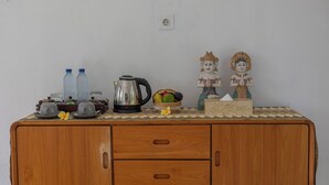 A wooden cabinet with two drawers, a kettle, two water bottles, a fruit bowl, and two decorative statues. - Radjes Bungalow Nusa Penida (Penida Island)