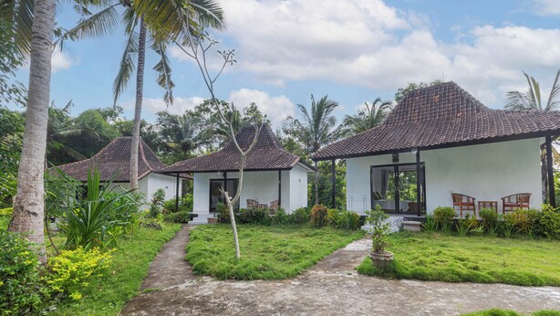 A bungalow with a tiled roof, surrounded by lush greenery and palm trees. - Radjes Bungalow Nusa Penida (Penida Island)