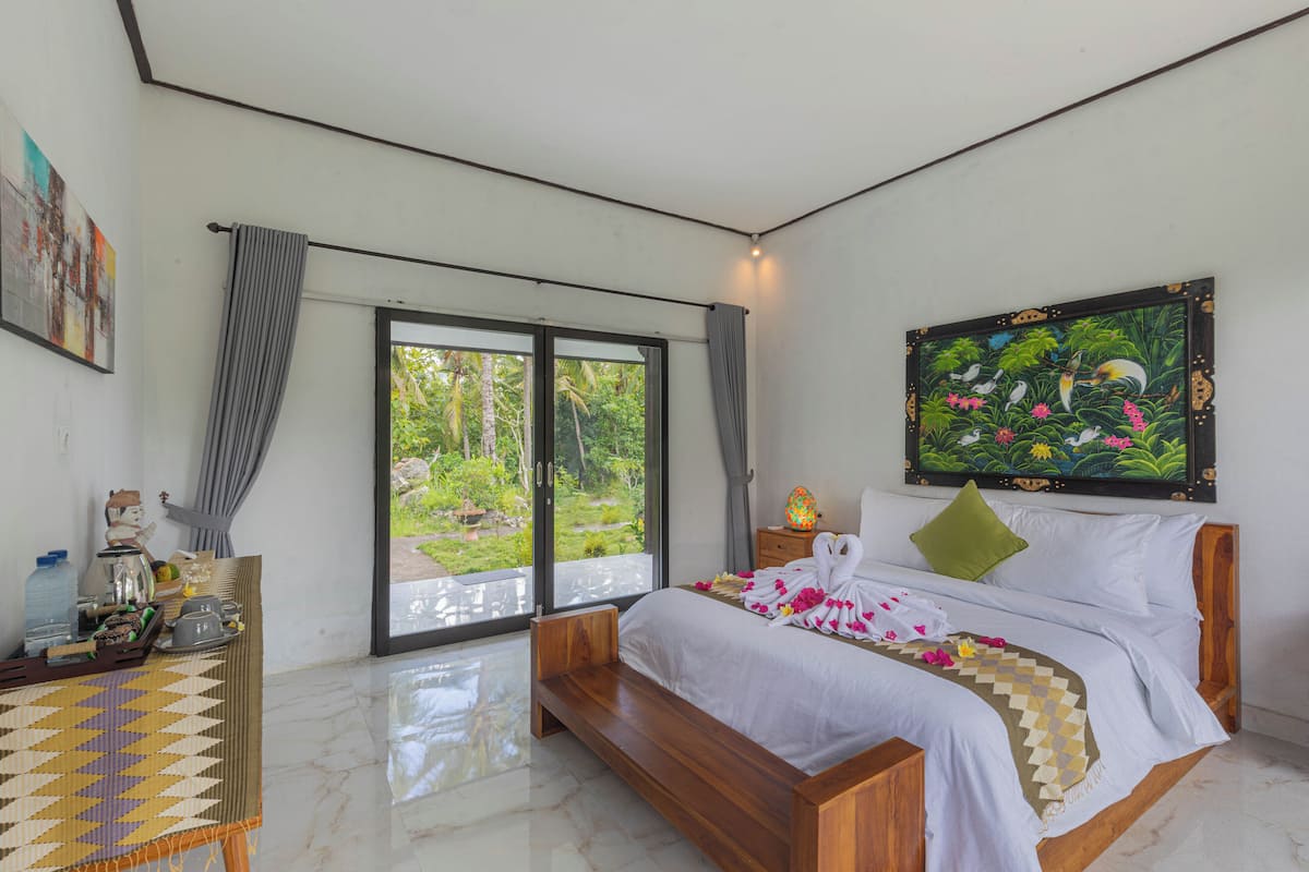 A bedroom with a bed, a window, a painting, and a bedside table.