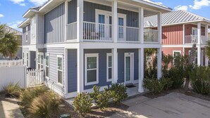 A two-story house with a balcony on the second floor, a white picket fence, and a small garden with shrubs and a palm tree. - 2 Master bedrooms, Steps to the beach, private pool (Panama City Beach)
