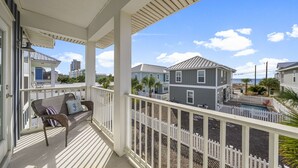A covered porch with a wicker chair and cushions, overlooking a residential area with houses and a pool. - 2 Master bedrooms, Steps to the beach, private pool (Panama City Beach)