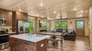 A spacious kitchen with wooden cabinets, a large island, stainless steel appliances, and a stone fireplace. - Luxury Cabin with Indoor Pool, Hot Tub, Views, Games, Fire Pit, Covered Decks! (Sevierville)
