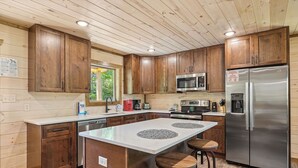 A modern kitchen with wooden cabinets, stainless steel appliances, and a central island with stools. - Luxury Cabin with Indoor Pool, Hot Tub, Views, Games, Fire Pit, Covered Decks! (Sevierville)