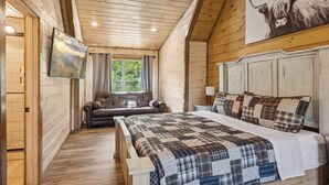 A wooden cabin bedroom with a large bed, a sofa, and a painting of a mountain landscape. - Luxury Cabin with Indoor Pool, Hot Tub, Views, Games, Fire Pit, Covered Decks! (Sevierville)