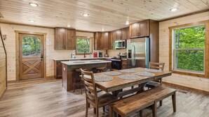 A wooden cabin interior with a kitchen, dining area, and large windows. - Luxury Cabin with Indoor Pool, Hot Tub, Views, Games, Fire Pit, Covered Decks! (Sevierville)