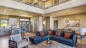 A spacious living area with a large sofa, a coffee table, and a dining area with wooden furniture. - Luxury 4 BR Cabin overlooking valley w/ Hot Tub, Game Room, Outdoor Fireplace (Sevierville)