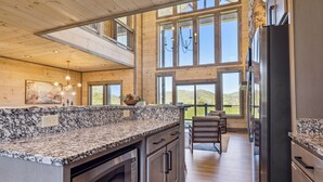 A spacious kitchen with granite countertops, stainless steel appliances, and large windows offering a view of the outdoors. - Luxury 4 BR Cabin overlooking valley w/ Hot Tub, Game Room, Outdoor Fireplace (Sevierville)