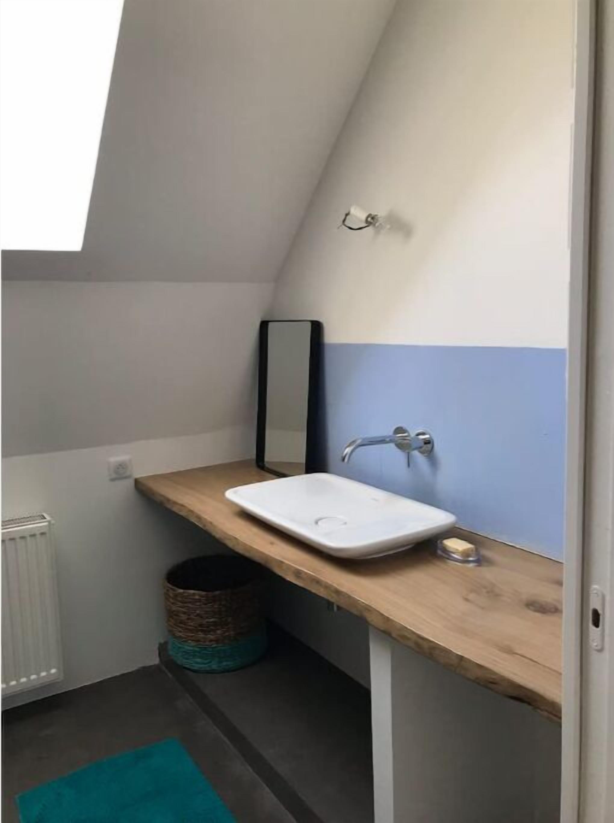 A small bathroom with a white sink, a wooden countertop, a mirror, and a blue wall.