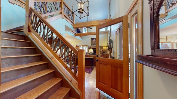 A wooden staircase with a railing, leading to a room with a stone fireplace and a lamp.