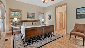 A bedroom with a wooden bed, a ceiling fan, a rug, and a chair. - The Lodge That Ruins Every Other Rental For You | Laughing Bear Lodge (Highlands)