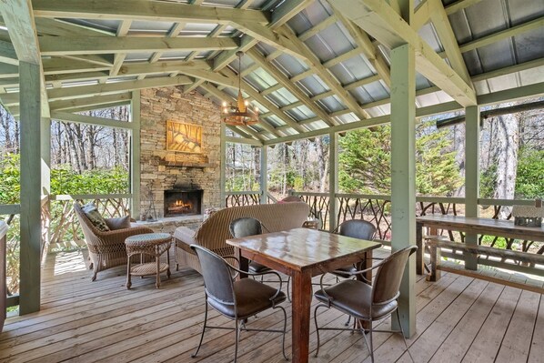 A covered outdoor seating area with a stone fireplace, wooden deck, and wicker furniture.