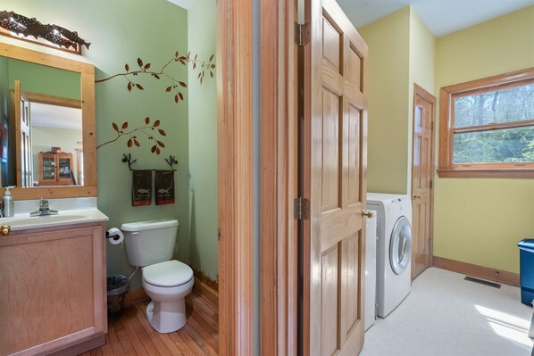 Un baño con tocador de madera, inodoro, lavadora y ventana.