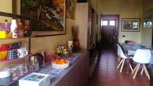 A kitchen with a counter, a dining table with chairs, a refrigerator, and a painting on the wall. - Affitacamere Domo - Luci (Nurachi)