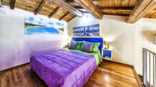 A bedroom with a wooden ceiling, a purple bed, a nightstand, and two paintings on the wall. - Affitacamere Domo - Luci (Nurachi)