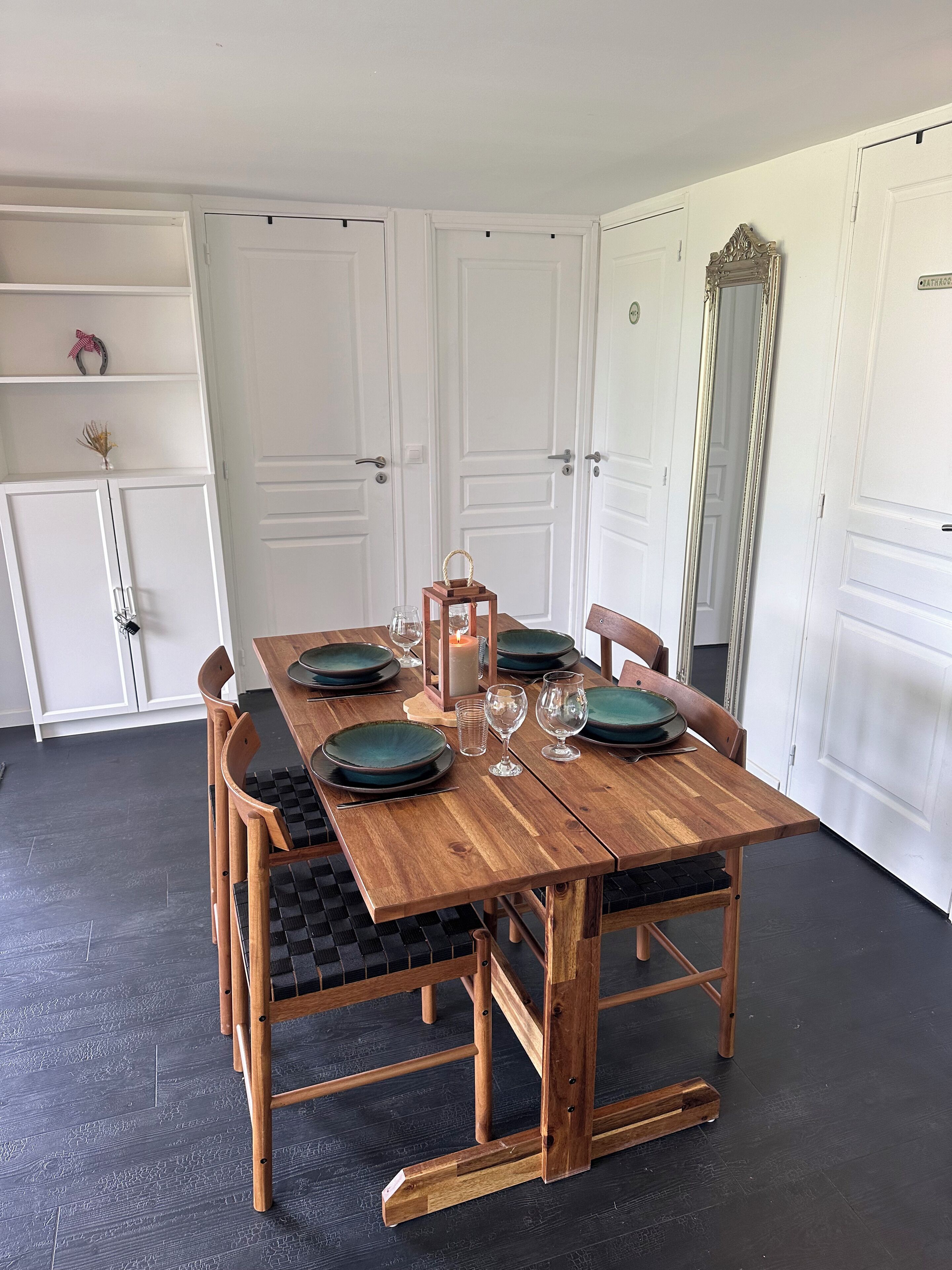 Una mesa de comedor con sillas, una vela y cristalería dispuesta en una habitación con puertas blancas y un espejo.