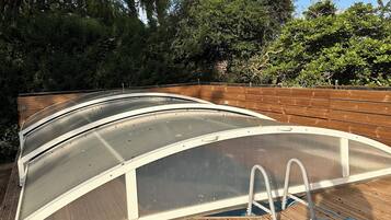 Una terrazza in legno con area piscina, circondata da alberi e un cielo sereno.