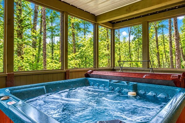 A hot tub with a view of a forest through large windows.