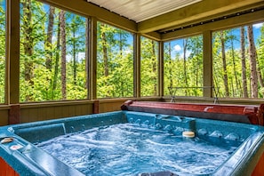 A hot tub with a view of a forest through large windows.