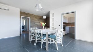 Un comedor moderno con una mesa y sillas blancas, un jarrón con flores y una cocina visible a través de una puerta abierta.