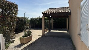 Un espacio al aire libre techado, con piso de baldosas y plantas en macetas.