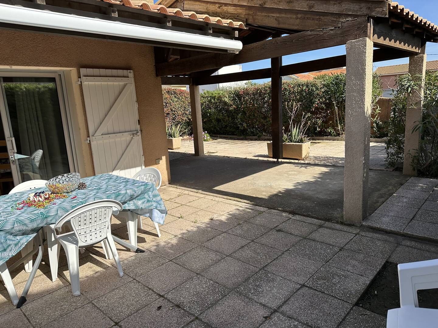 An outdoor patio with a table and chairs, a covered area, and a view of the surrounding garden.
