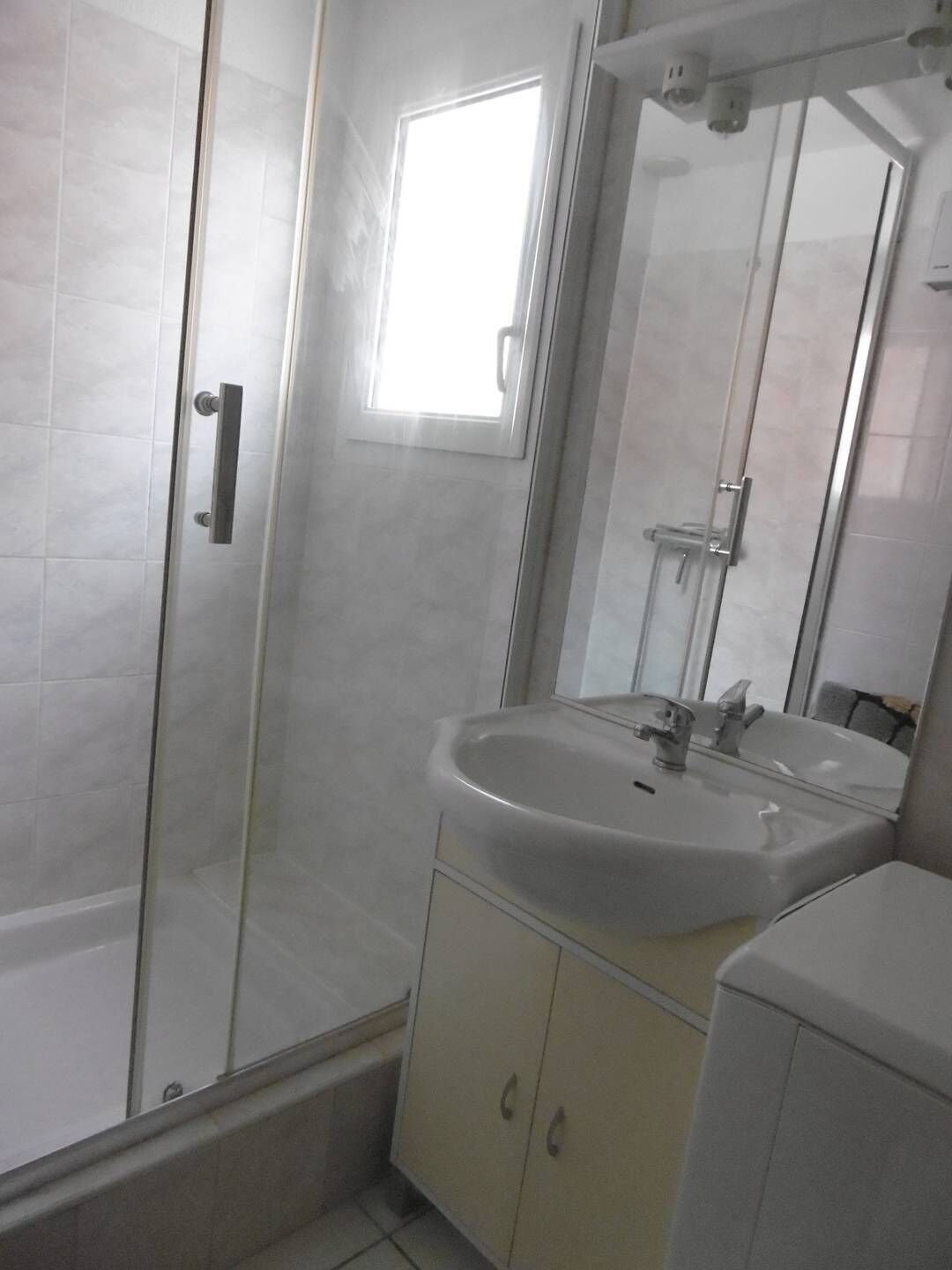 Un baño con cabina de ducha de vidrio, un lavabo con espejo y una ventana que proporciona luz natural.