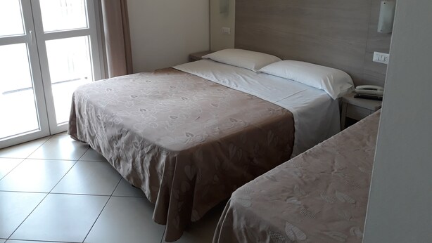 A hotel room with a bed, bedside table, and a window with curtains.
