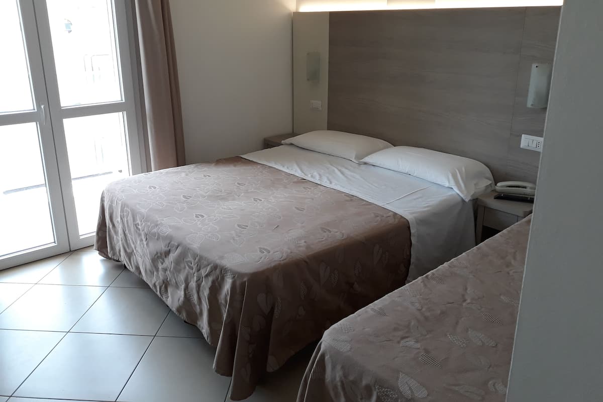 A hotel room with a bed, bedside table, and a window with curtains.