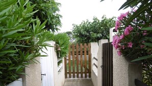 Une entrée fermée par un portail, avec un chemin en béton qui traverse un jardin.
