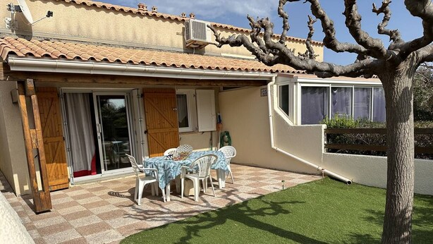 Une maison dotée d’un patio comprenant une table et des chaises, une porte en bois et un arbre.
