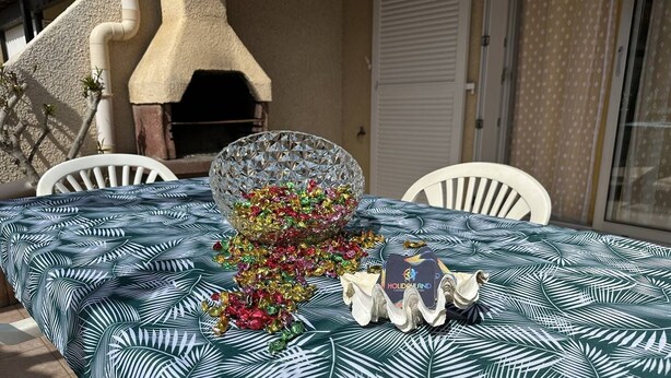Una mesa dispuesta al aire libre con un mantel estampado, un cuenco de vidrio decorativo y una tarjeta.