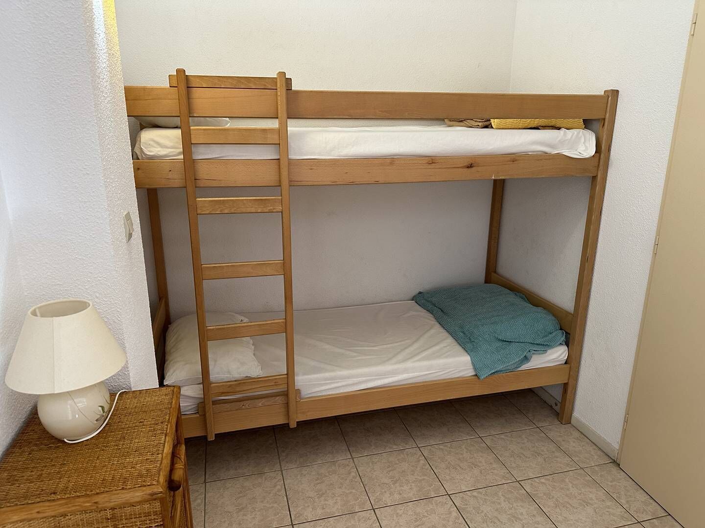 A bunk bed with a ladder, a bedside table with a lamp, and a small rug.