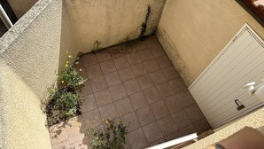 Un espacio al aire libre pequeño con suelo de baldosas, una puerta blanca y algunas plantas.