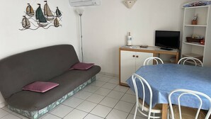 Una habitación con sofá, una mesa de comedor con sillas, un televisor y una estantería con objetos.