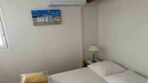 Una habitación pequeña y limpia con una cama, una mesita de noche, una lámpara y un cuadro en la pared.