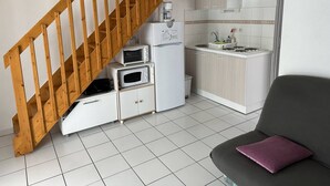 Una cocina compacta con una escalera de madera, armarios blancos, un microondas, un refrigerador y un lavamanos.