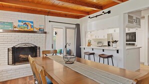 A dining area with a wooden table, chairs, a fireplace, and a kitchen with white cabinets and appliances. - Sweet Escape | Family Retreat | Vibrant  | Spa (San Diego)