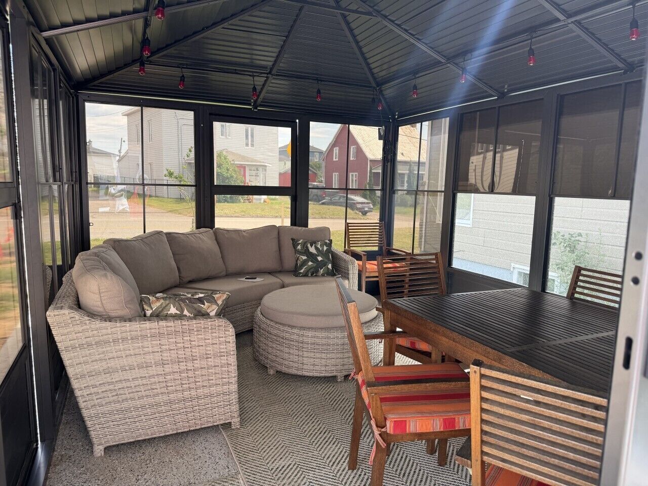 A covered patio area with a sectional sofa, ottoman, dining table, and chairs.