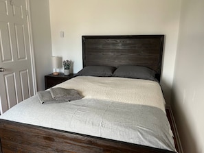 Un lit avec une tête de lit sombre, une couvre-lit beige et deux oreillers.