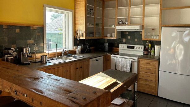 A kitchen with wooden cabinets, a white refrigerator, and a window with a view of greenery. - Le Havre du Pilote Aux Bergeronnes (Grandes-Bergeronnes)