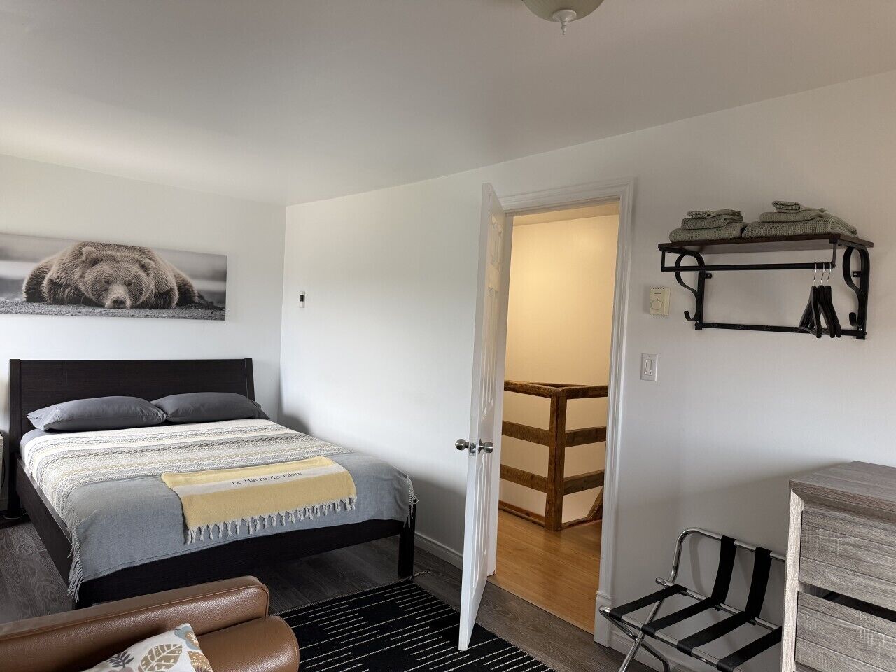 A bedroom with a bed, a door leading to a wooden staircase, and a wall-mounted shelf with towels.