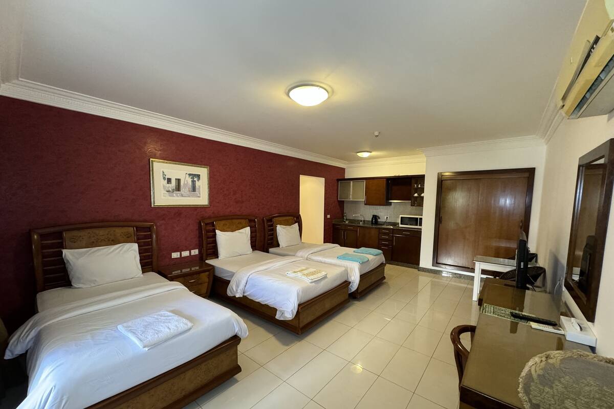 A hotel room with two beds, a kitchenette, a dining table, and a TV.