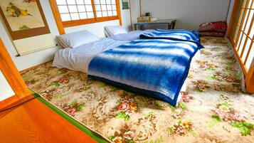 Una habitación tradicional japonesa con suelo de tatami, una cama baja de madera con manta azul y una ventana con puertas correderas shoji.