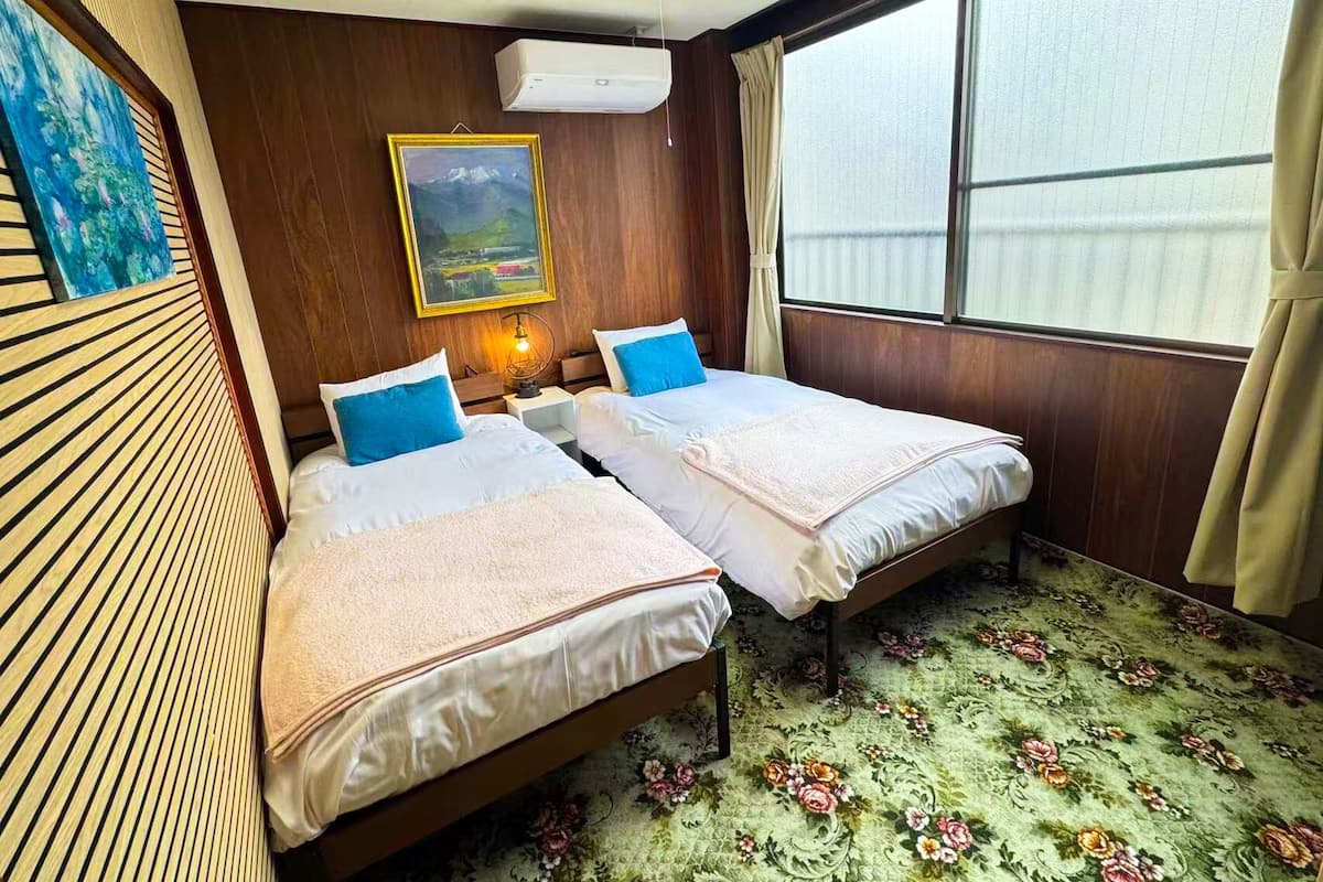 A room with two beds, a painting on the wall, and a window with curtains.