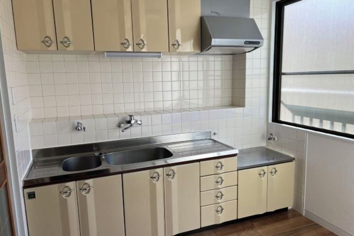 A kitchen with white tiled backsplash, stainless steel sink, beige cabinets, and a window with blinds.