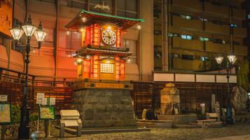 A traditional Japanese lantern structure with a clock, surrounded by stone lanterns and a stone statue.