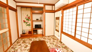 A traditional Japanese room with tatami flooring, a low wooden table, sliding doors, and a television on a shelf. - Himerakuen (Matsuyama)