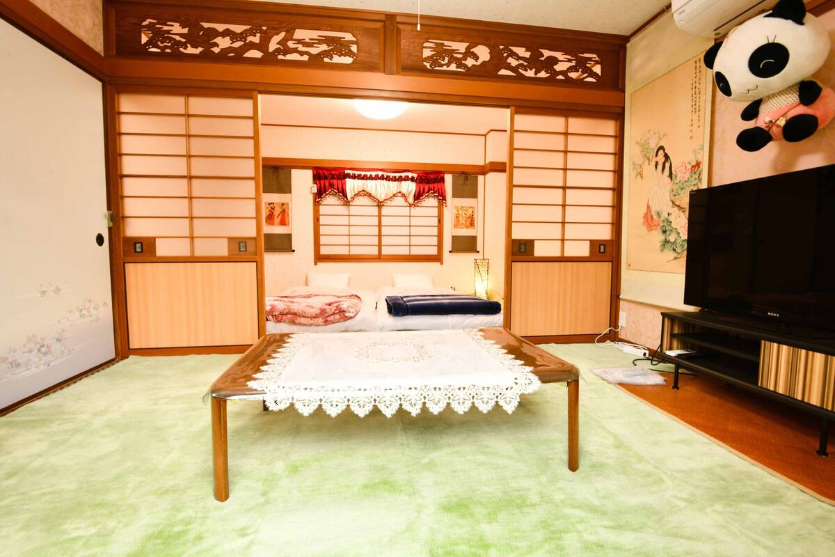 A traditional Japanese room with tatami flooring, a low wooden table, a television, and a panda plush toy.