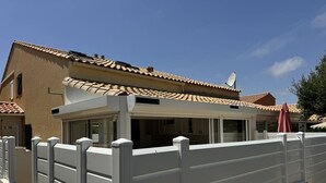 A residential building with a tiled roof, a covered patio area, and a white fence.
