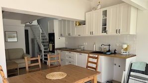 A compact kitchen with white cabinets, a wooden dining table, and a staircase leading to a loft.